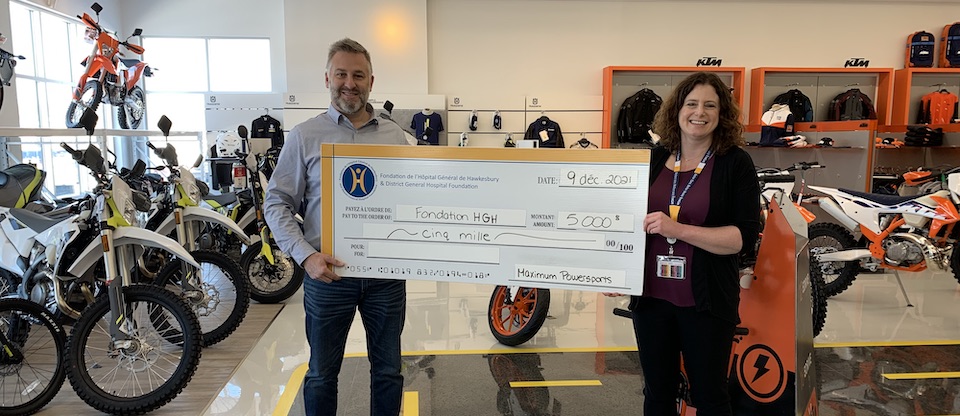 Surrounded by motorcyles at Maximum Powersports, Kevin Assaly hands a giant $5,000 cheque to Erin Tabakman, Executive Director of the HGH Foundation.