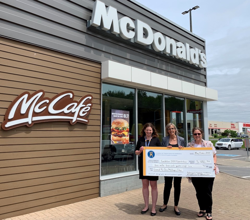Two HGH Foundation reps receive giant cheque from McDonald's rep in front of restaurant