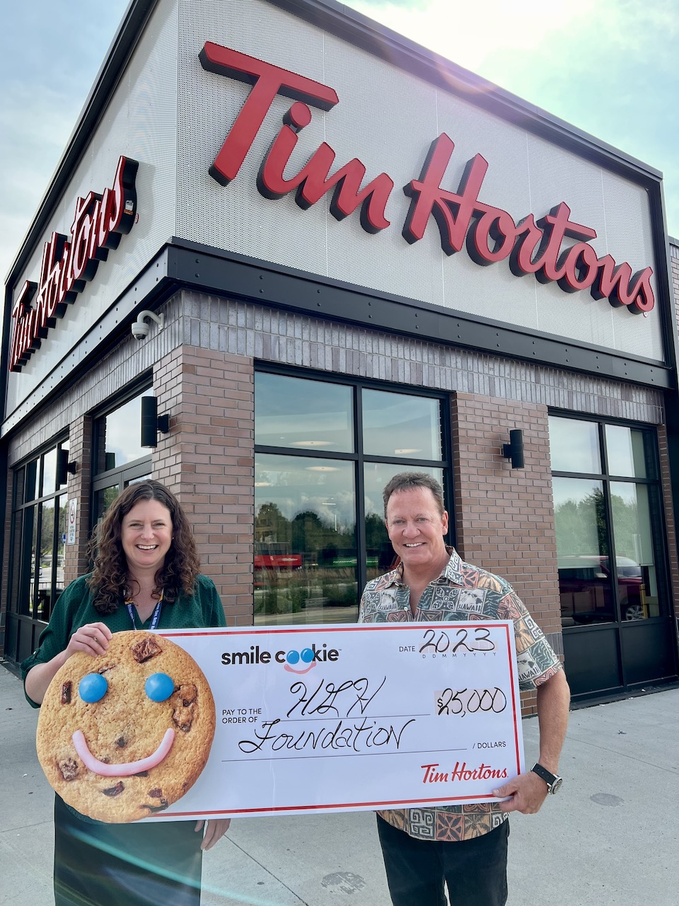 Erin Tabakman and Tim Hortons representative hold a $25,000 giant cheque