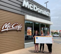 Deux représentantes de la Fondation HGH reçoivent un chèque géant d'une représentante de McDonald's devant le restaurant